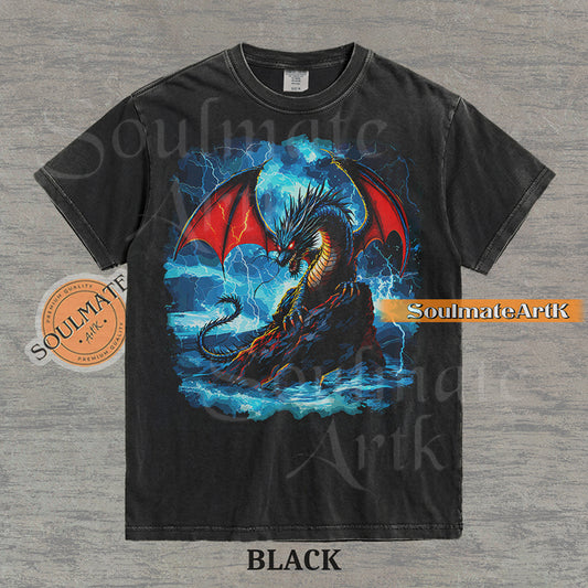 Vintage-style fantasy graphic of a black dragon with red wings perched on a rock amidst blue lightning and ocean waves on a washed black t-shirt.