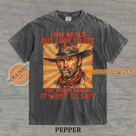 Graphic of a cowboy with a cigar and sunburst background with text "I may be old but I got to see the world before it went to sh!t" on a washed pepper t-shirt.