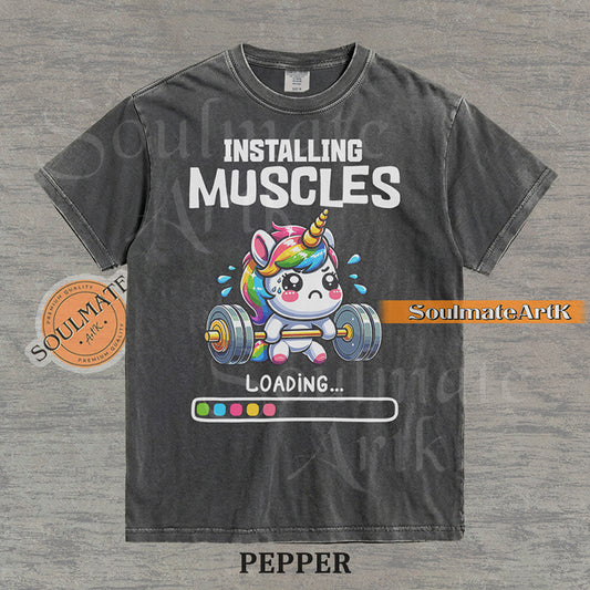 Cute cartoon unicorn lifting a heavy barbell with a loading bar and text reading Installing Muscles on a washed pepper shirt.