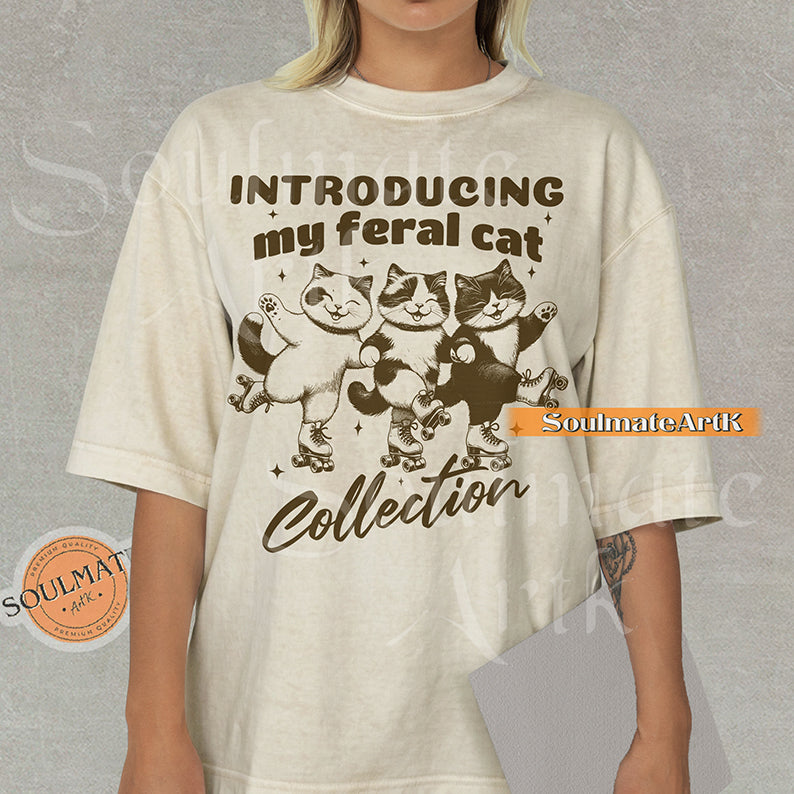 Hand-drawn illustration of three tuxedo cats on roller skates with the text "Introducing my feral cat Collection" on a natural shirt.