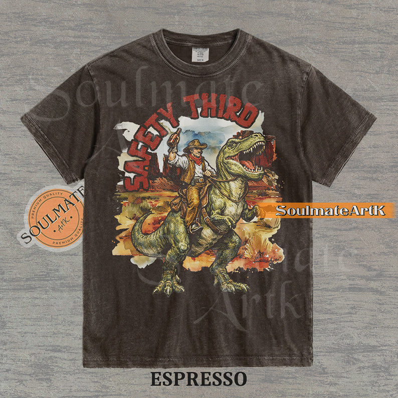 Vintage-style graphic of a cowboy with a hat and drink riding a T-Rex through a desert landscape with red text reading Safety Third on a washed espresso t-shirt.