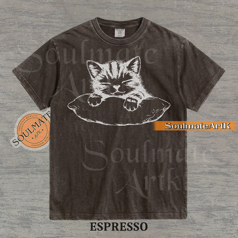 Hand-drawn sketch of a striped kitten sleeping on a pillow in black ink on a espresso vintage-wash t-shirt.