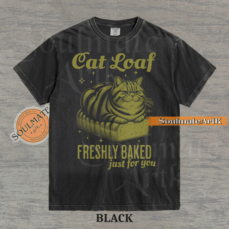 Illustration of a tabby cat sitting on a loaf of bread with text reading "Cat Loaf Freshly Baked just for you" on a washed black t-shirt.
