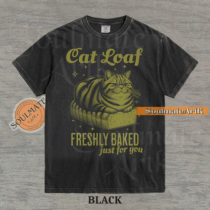 Illustration of a tabby cat sitting on a loaf of bread with text reading "Cat Loaf Freshly Baked just for you" on a washed black t-shirt.