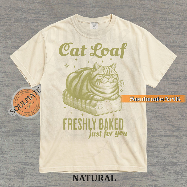 Illustration of a tabby cat sitting on a loaf of bread with text reading "Cat Loaf Freshly Baked just for you" on a washed natural t-shirt.
