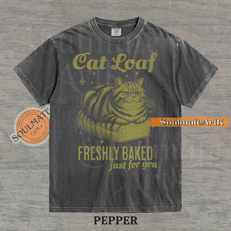 Illustration of a tabby cat sitting on a loaf of bread with text reading "Cat Loaf Freshly Baked just for you" on a washed pepper t-shirt.