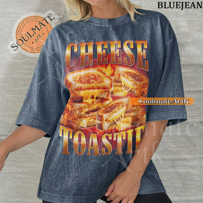 Graphic collage of melting grilled cheese sandwiches surrounded by flames with bold metallic text reading CHEESE TOASTIE on a washed bluejean shirt.