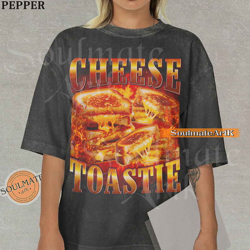 Graphic collage of melting grilled cheese sandwiches surrounded by flames with bold metallic text reading CHEESE TOASTIE on a washed pepper shirt.
