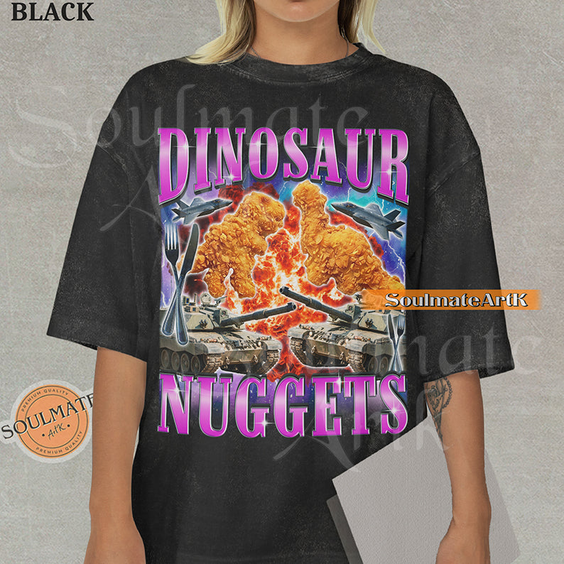 Vintage-style action graphic of dinosaur nuggets surrounded by tanks, fighter jets, and explosions with pink metallic text on a washed black t-shirt.