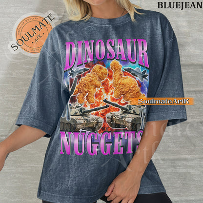 Vintage-style action graphic of dinosaur nuggets surrounded by tanks, fighter jets, and explosions with pink metallic text on a washed bluejean t-shirt.