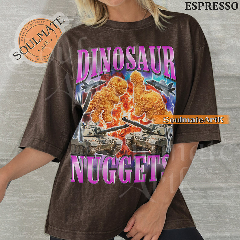 Vintage-style action graphic of dinosaur nuggets surrounded by tanks, fighter jets, and explosions with pink metallic text on a washed espresso t-shirt.