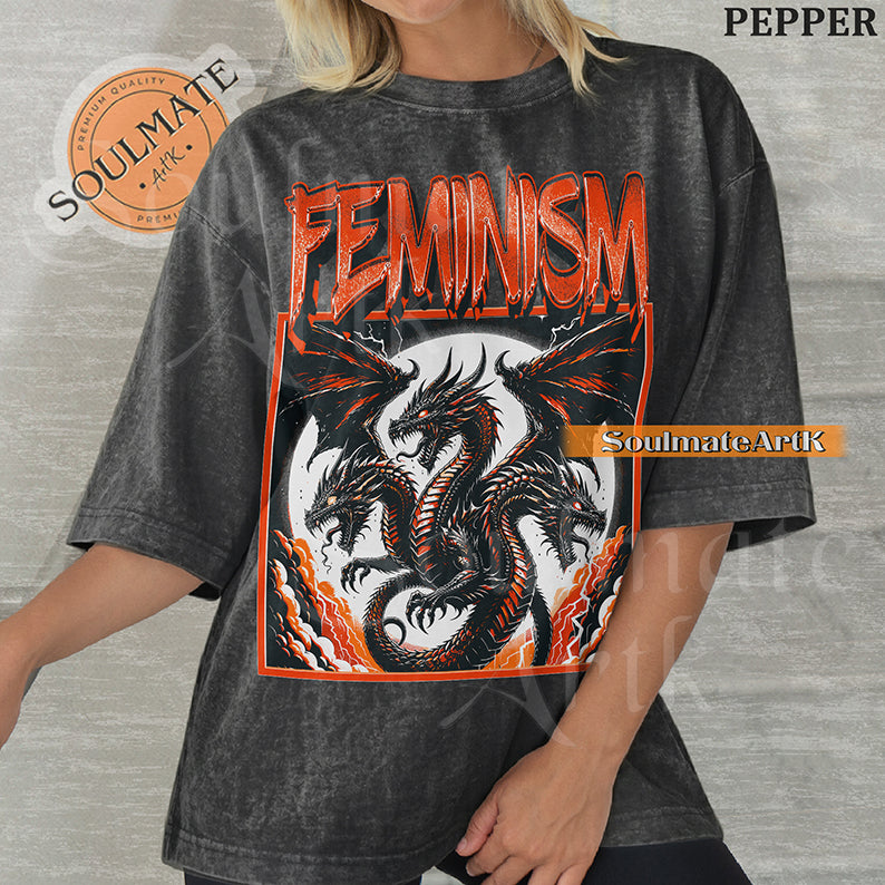 Illustration of a multi-headed red and black dragon in a framed graphic with bold red text reading Feminism on a washed pepper shirt.
