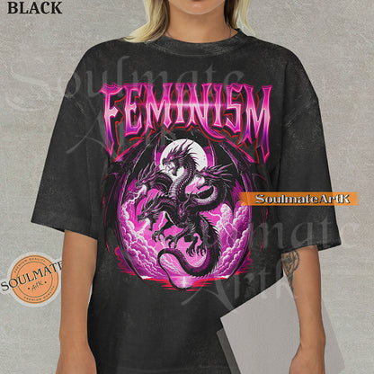 Illustration of a multi-headed black and purple dragon in front of a pink moon with bold purple text reading Feminism on a black colored shirt.