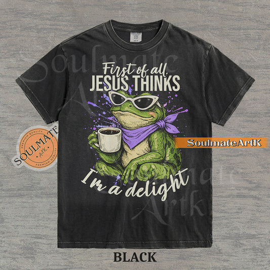 Illustration of a green frog in sunglasses and a purple scarf holding a coffee mug with the text "First of all, Jesus thinks I'm a delight" on a washed black shirt.