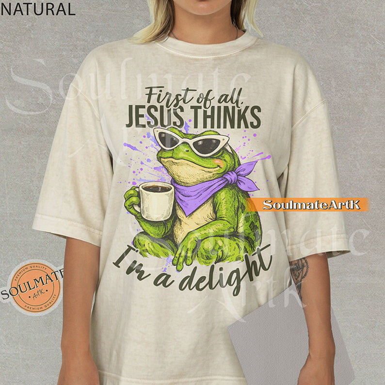 Illustration of a green frog in sunglasses and a purple scarf holding a coffee mug with the text "First of all, Jesus thinks I'm a delight" on a washed natural shirt.
