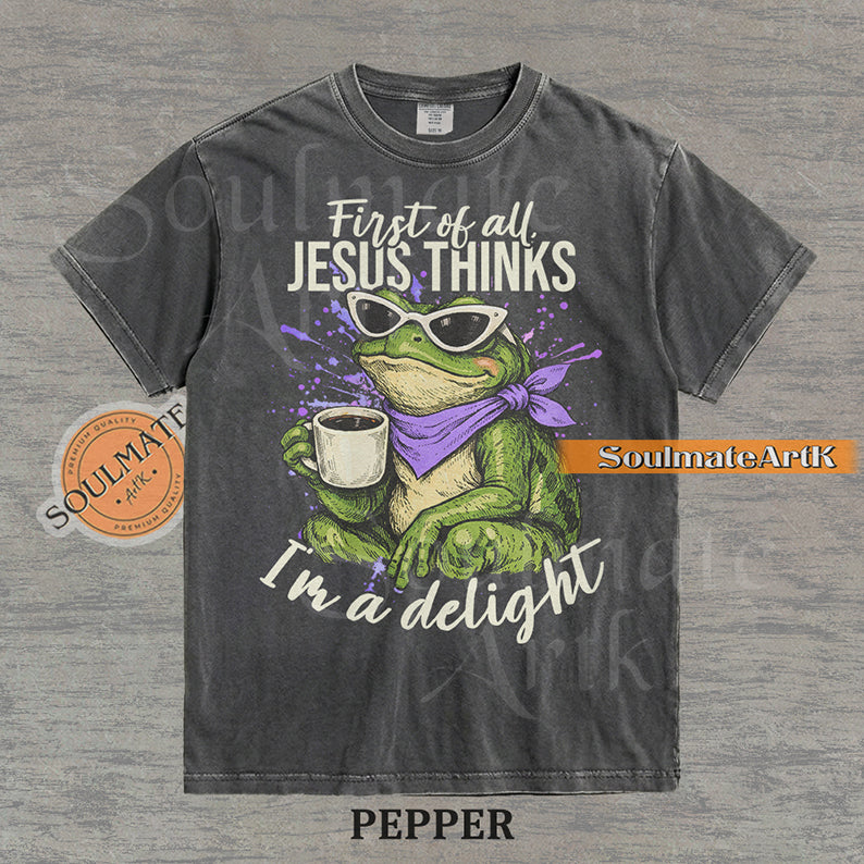 Illustration of a green frog in sunglasses and a purple scarf holding a coffee mug with the text "First of all, Jesus thinks I'm a delight" on a washed pepper shirt.