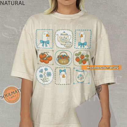 Cottagecore grid illustration featuring geese with bows, strawberries, tomatoes, and vintage teapots on a natural t-shirt.