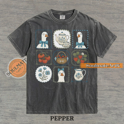 Cottagecore grid illustration featuring geese with bows, strawberries, tomatoes, and vintage teapots on a washed pepper t-shirt.