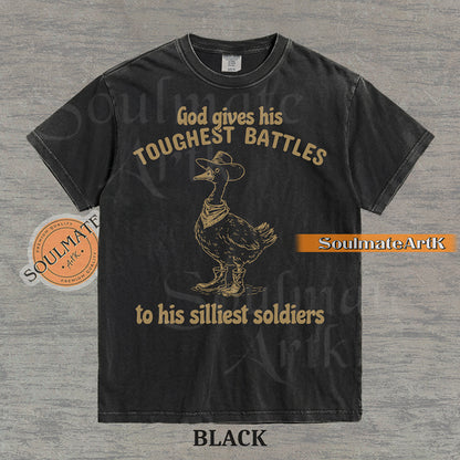 Vintage-style illustration of a goose wearing a cowboy hat, bandana, and boots with the text God gives his toughest battles to his silliest soldiers on a washed Comfort Colors t-shirt.
