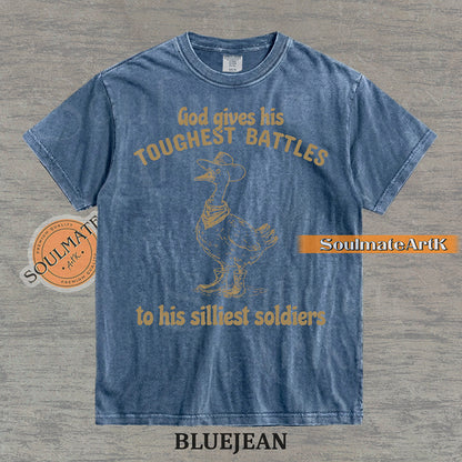 Vintage-style illustration of a goose wearing a cowboy hat, bandana, and boots with the text God gives his toughest battles to his silliest soldiers on a washed Comfort Colors t-shirt.