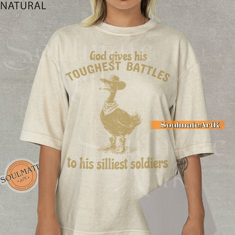 Vintage-style illustration of a goose wearing a cowboy hat, bandana, and boots with the text God gives his toughest battles to his silliest soldiers on a washed Comfort Colors t-shirt.