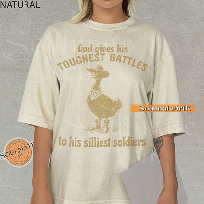 Vintage-style illustration of a goose wearing a cowboy hat, bandana, and boots with the text God gives his toughest battles to his silliest soldiers on a washed Comfort Colors t-shirt.
