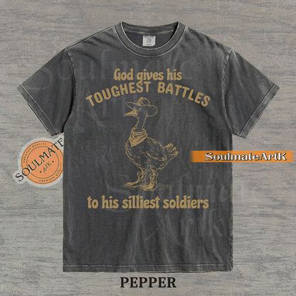 Vintage-style illustration of a goose wearing a cowboy hat, bandana, and boots with the text God gives his toughest battles to his silliest soldiers on a washed Comfort Colors t-shirt.