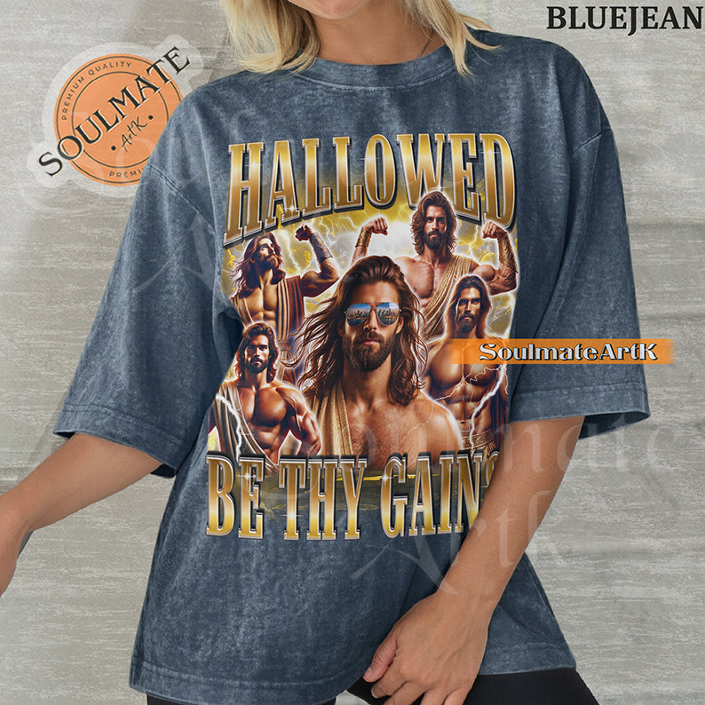 Vintage-style collage of a muscular man with a beard and sunglasses surrounded by lightning with bold gold metallic text reading Hallowed Be Thy Gains on a washed bluejean t-shirt.