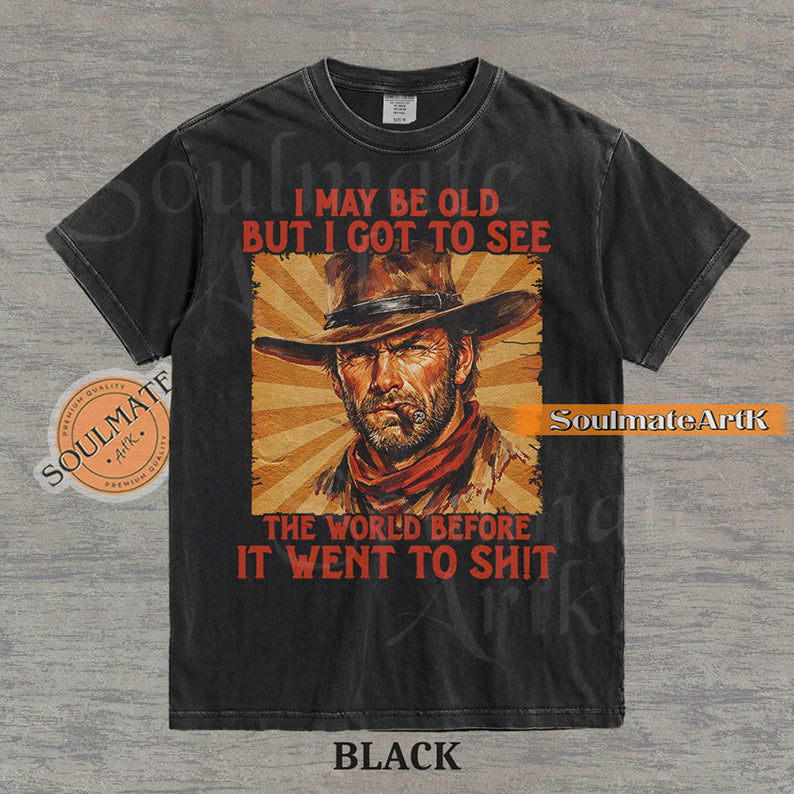 Graphic of a cowboy with a cigar and sunburst background with text "I may be old but I got to see the world before it went to sh!t" on a washed black t-shirt.