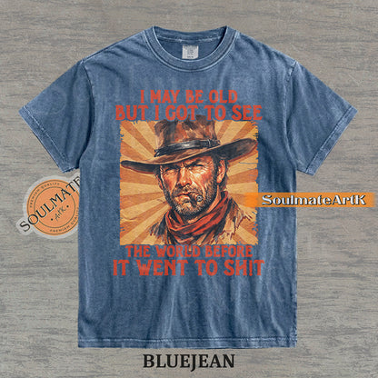 Graphic of a cowboy with a cigar and sunburst background with text "I may be old but I got to see the world before it went to sh!t" on a washed bluejean t-shirt.