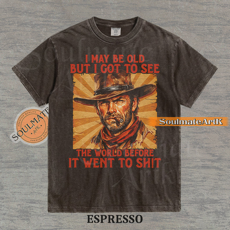 Graphic of a cowboy with a cigar and sunburst background with text "I may be old but I got to see the world before it went to sh!t" on a washed espresso t-shirt.