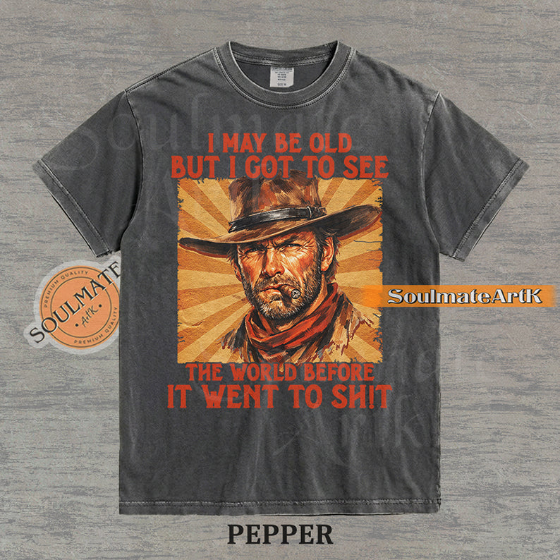 Graphic of a cowboy with a cigar and sunburst background with text "I may be old but I got to see the world before it went to sh!t" on a washed pepper t-shirt.