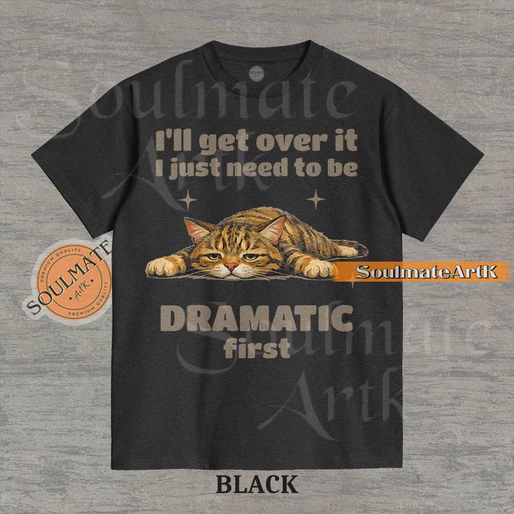 A funny t-shirt featuring a cartoon cat laying flat on the floor with the text "I'll Get Over It I Just Need To Be Dramatic First." The design is an ironic, unhinged meme style.