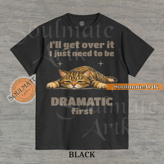 A funny t-shirt featuring a cartoon cat laying flat on the floor with the text "I'll Get Over It I Just Need To Be Dramatic First." The design is an ironic, unhinged meme style.