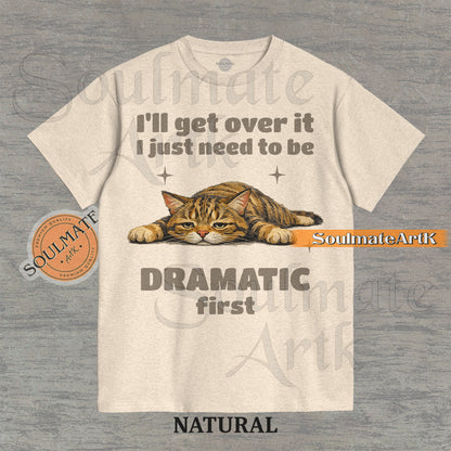 A funny t-shirt featuring a cartoon cat laying flat on the floor with the text "I'll Get Over It I Just Need To Be Dramatic First." The design is an ironic, unhinged meme style.