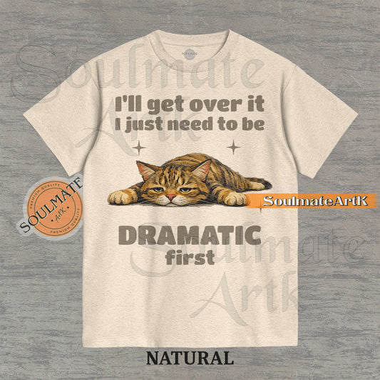 A funny t-shirt featuring a cartoon cat laying flat on the floor with the text "I'll Get Over It I Just Need To Be Dramatic First." The design is an ironic, unhinged meme style.