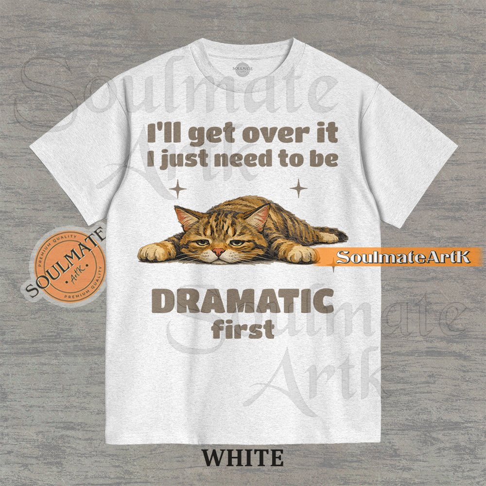 A funny t-shirt featuring a cartoon cat laying flat on the floor with the text "I'll Get Over It I Just Need To Be Dramatic First." The design is an ironic, unhinged meme style.