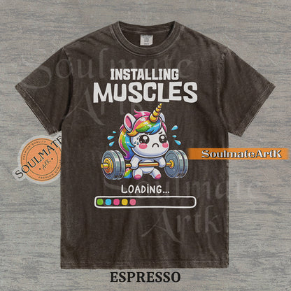 Cute cartoon unicorn lifting a heavy barbell with a loading bar and text reading Installing Muscles on a washed espresso shirt.