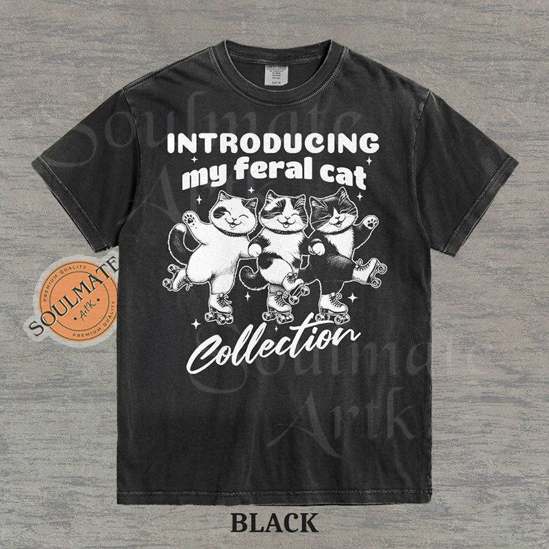 Hand-drawn illustration of three tuxedo cats on roller skates with the text "Introducing my feral cat Collection" on a washed black shirt.