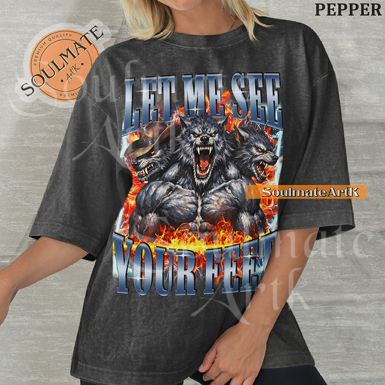 Graphic of three muscular werewolves surrounded by fire and lightning with bold blue text reading LET ME SEE YOUR FEET on a washed pepper shirt.