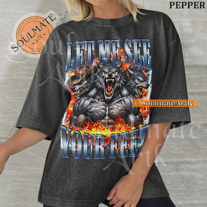 Graphic of three muscular werewolves surrounded by fire and lightning with bold blue text reading LET ME SEE YOUR FEET on a washed pepper shirt.