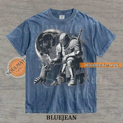Detailed illustration of a kneeling medieval knight petting a raccoon in front of a giant moon on a washed bluejean shirt.