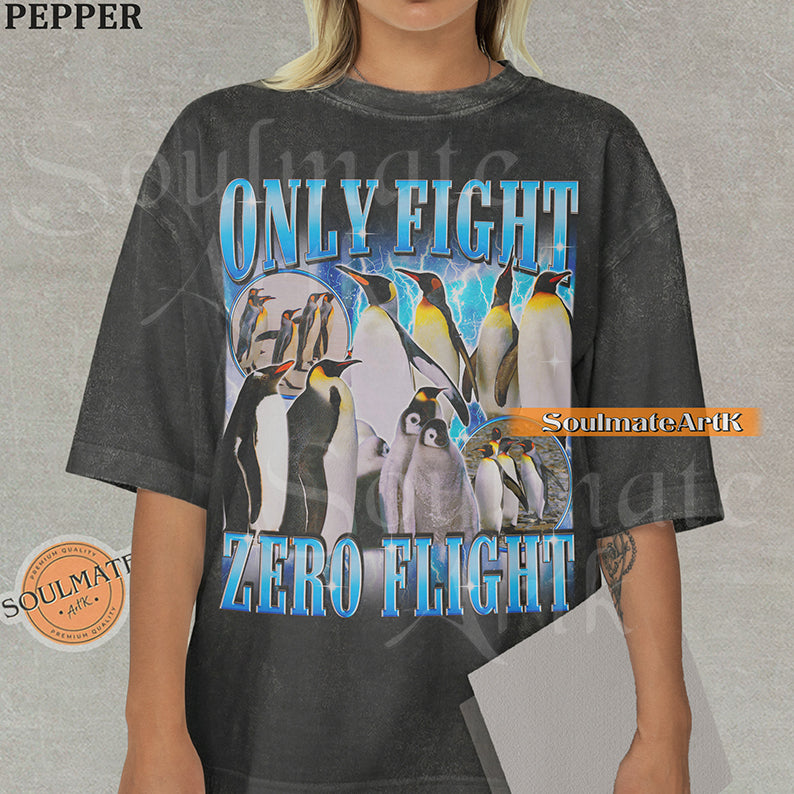 Graphic collage of emperor penguins and chicks with blue lightning and bold metallic text reading ONLY FIGHT ZERO FLIGHT on a washed pepper t-shirt.