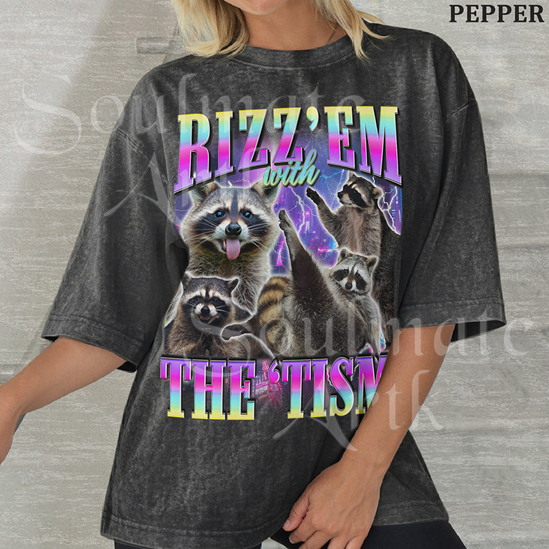 Graphic collage of multiple raccoons over a neon city with bold rainbow text reading RIZZ 'EM WITH THE 'TISM on a washed pepper shirt.