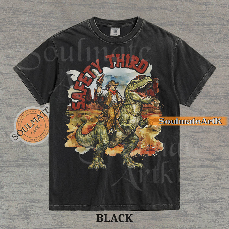 Vintage-style graphic of a cowboy with a hat and drink riding a T-Rex through a desert landscape with red text reading Safety Third on a washed black t-shirt.