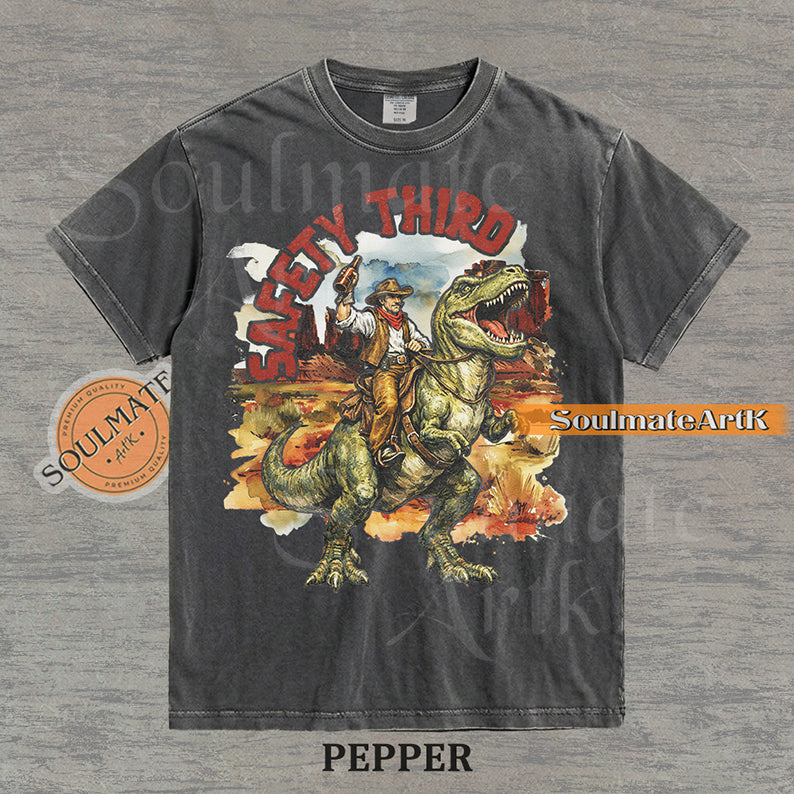 Vintage-style graphic of a cowboy with a hat and drink riding a T-Rex through a desert landscape with red text reading Safety Third on a washed pepper t-shirt.