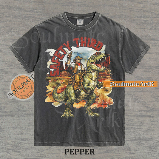 Vintage-style graphic of a cowboy with a hat and drink riding a T-Rex through a desert landscape with red text reading Safety Third on a washed pepper t-shirt.
