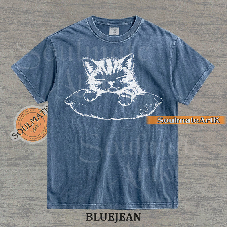 Hand-drawn sketch of a striped kitten sleeping on a pillow in black ink on a bluejean vintage-wash t-shirt.