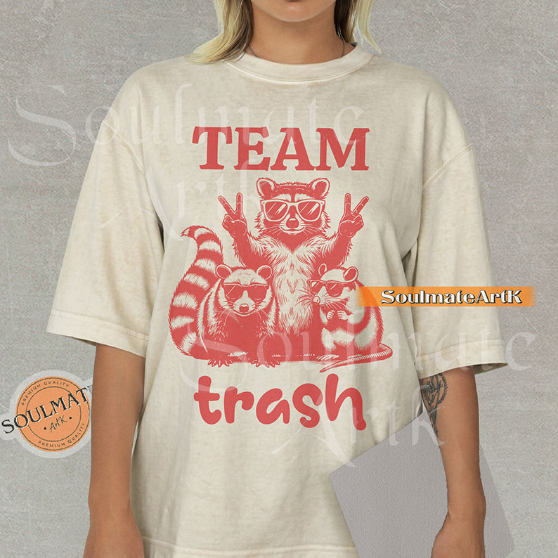 Illustration of a raccoon and two opossums wearing sunglasses with the text "TEAM trash" in red on a natural shirt.
