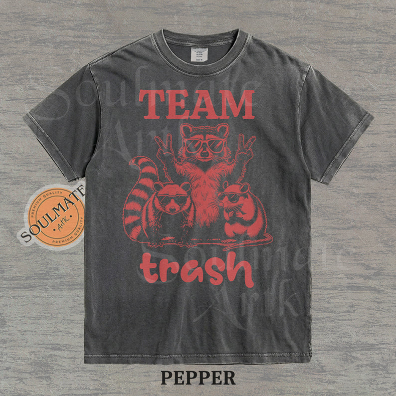 Illustration of a raccoon and two opossums wearing sunglasses with the text "TEAM trash" in red on a washed pepper shirt.